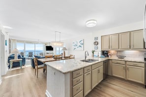 A spacious kitchen with a large island, a dining area with a view, and a living room with a sofa and chairs.