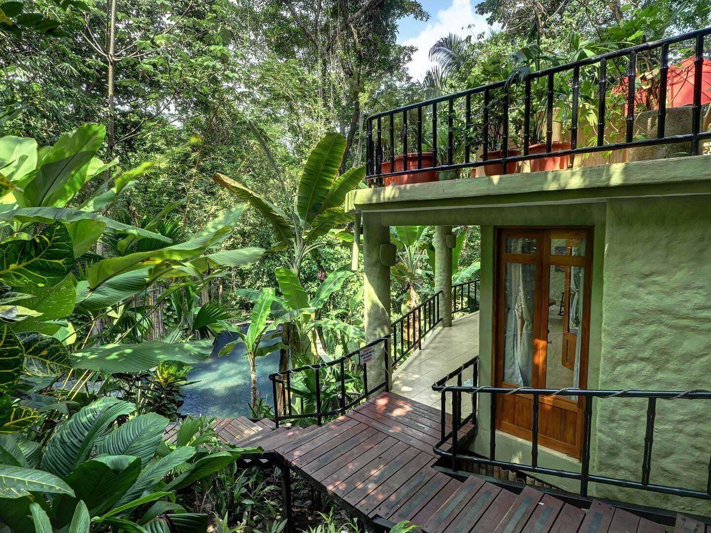 A two-story building with a balcony, surrounded by lush greenery and a small water feature.