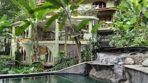 Un exuberante jardín interior con cascada, piscina y un edificio de varios pisos con balcones.