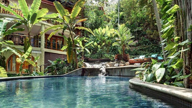Una piscina con cascada rodeada de exuberante vegetación tropical.