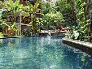Ein Pool mit Wasserfall, umgeben von üppiger tropischer Vegetation.
