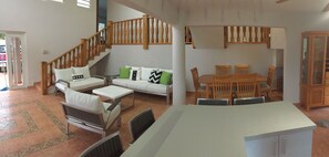 Ein geräumiger Wohnbereich mit einem weißen Sofa, grünen Kissen, einem Holzespeisetisch mit Stühlen und einer Treppe mit Holzläufer.