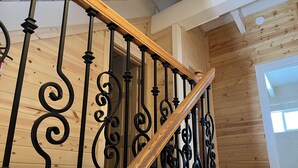 Interior de madera con una escalera que presenta barandillas de metal negro ornamentado y un pasamanos de madera.