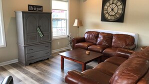 A living room with a brown leather sofa, a wooden coffee table, a gray cabinet, and a wall clock.