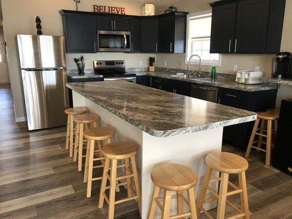 Una cocina moderna con un refrigerador de acero inoxidable, un microondas integrado, un horno doble y una encimera de granito. Hay taburetes de madera alrededor de la isla.