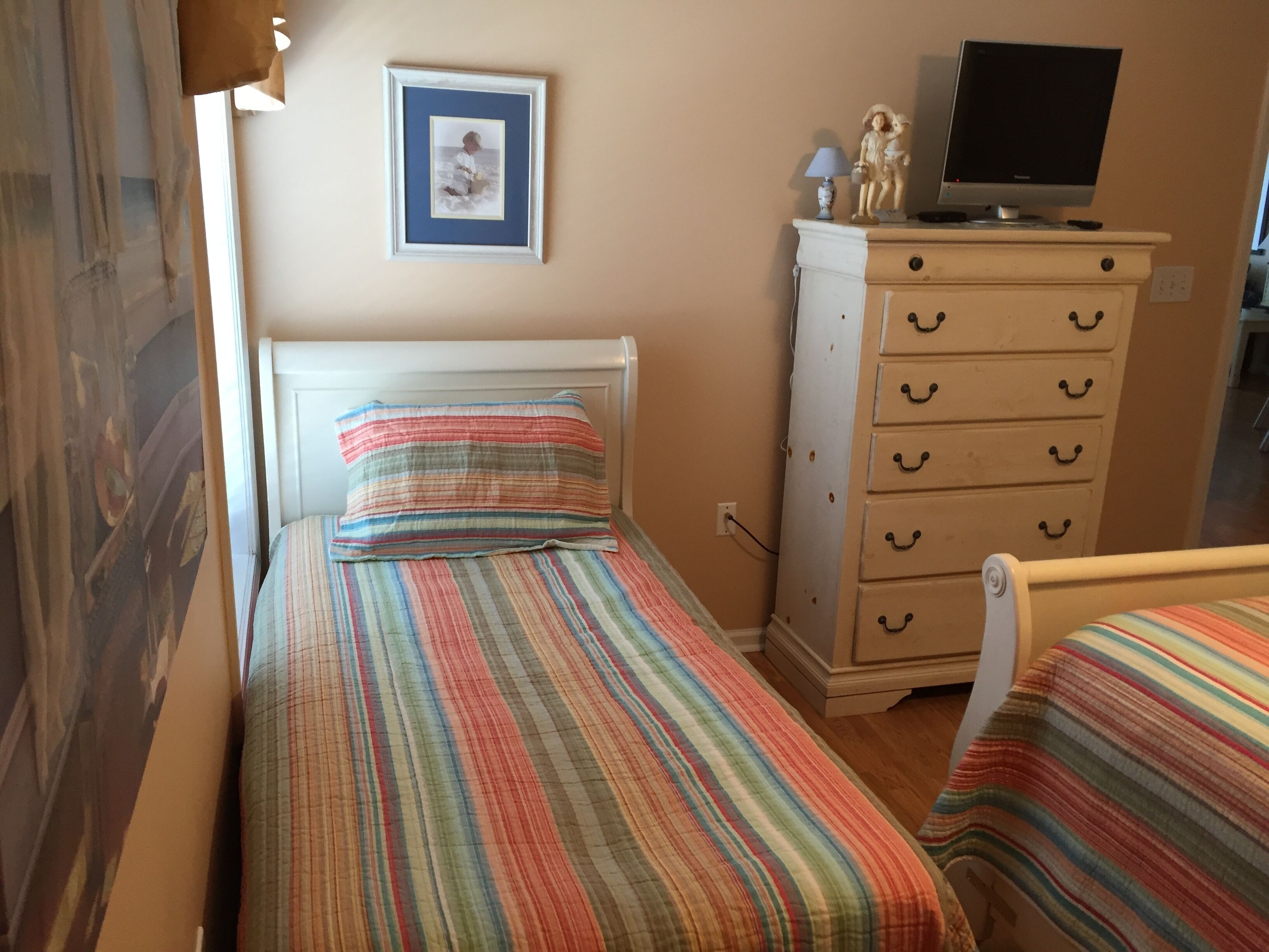 A bedroom with a bed, a dresser, a television, and a framed picture on the wall.