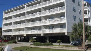 A multi-story hotel with balconies, a parking area, and a small garden.