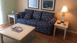 A living room with a blue sofa, a white coffee table, two framed pictures on the wall, a lamp on a side table, and a small table with a model ship.