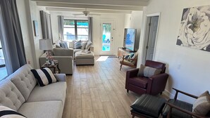A spacious living room with a beige sofa, a red armchair, and a wooden coffee table. A television is mounted on the wall, and there is a painting above it. -  Private Heated Pool Beach Home 2/2 Sleeps 6 Pets ok Perfect Location (St Pete Beach)
