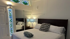 A neatly made bed with a grey blanket, two pillows, and a throw blanket. There is a nightstand with two lamps and a mirror above the bed. The room has white walls and a wooden headboard. -  Private Heated Pool Beach Home 2/2 Sleeps 6 Pets ok Perfect Location (St Pete Beach)