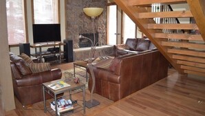 Un salón amplio con un sofá de cuero marrón, una mesa de centro de madera, un televisor y una chimenea.