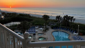 Zona de piscina en un resort con varios jacuzzis y sillas de descanso, con vistas a una playa al atardecer.