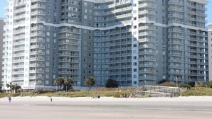 Un edificio residencial de varios pisos con balcones, cerca de una playa.