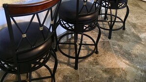 Una cocina con encimera de granito, pileta de acero inoxidable y tres taburetes negros con asientos de madera.