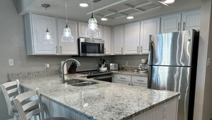 A kitchen with white cabinets, a stainless steel refrigerator, a granite countertop, and pendant lighting. - Seawatch Resort Oceanfront 2 BR - Large Balcony (Myrtle Beach)