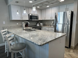 A kitchen with white cabinets, a stainless steel refrigerator, a granite countertop, and pendant lighting.