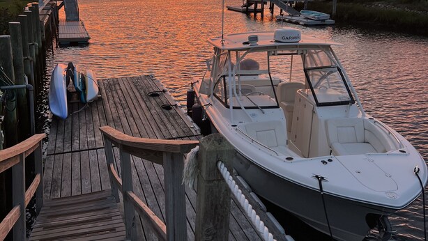 Een houten steiger met een boot aanmeren aan het einde, een klein pierje, en rustig water dat de zonsondergang weerspiegelt.
