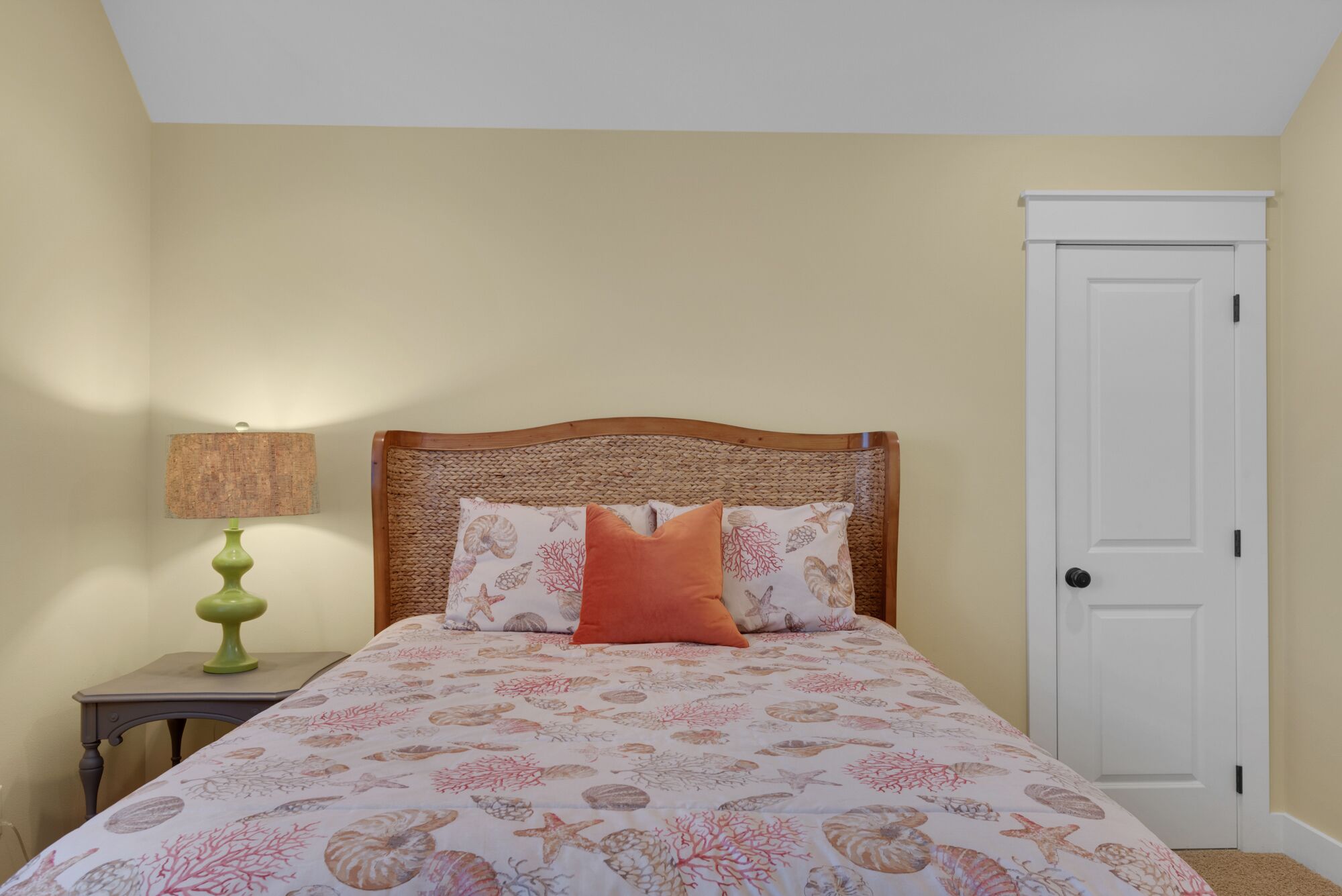 Um quarto com uma cama, mesa de cabeceira, abajur e porta.