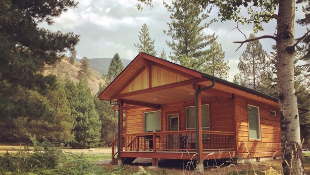 A wooden cabin with a porch, surrounded by trees and ferns. - More than just a cabin... Experience Montana Adventure (Trout Creek)