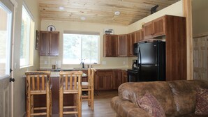 A kitchen with wooden cabinets, a black refrigerator, and a dining area with wooden chairs. - More than just a cabin... Experience Montana Adventure (Trout Creek)