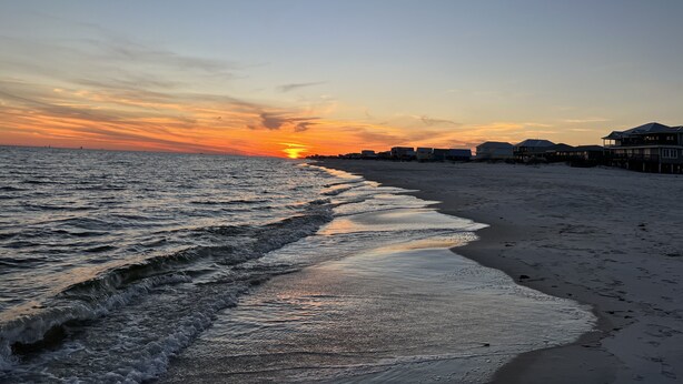 A beach with a sunset, waves, and beachfront houses. - Beautiful 6BR Gulf Front Home - "REST AREA WEST" - Pool & Deck - Reserve Now! (Gulf Shores)