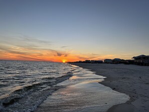 A beach with a sunset, waves, and beachfront houses.