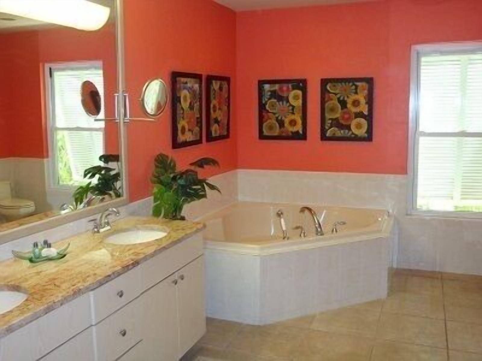 A bathroom with a large tub, a sink, and a mirror. There are two wall-mounted paintings and a potted plant.