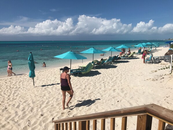 A beach with turquoise water, people sunbathing, and umbrellas.