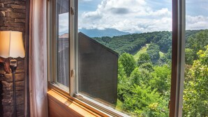 Quarto com uma grande janela que oferece vista de uma paisagem verdejante e montanhas.