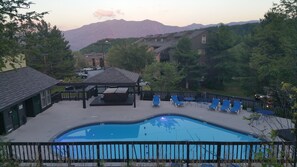 Una piscina con sillas de descanso, una zona de estar cubierta y vistas a montañas al fondo.