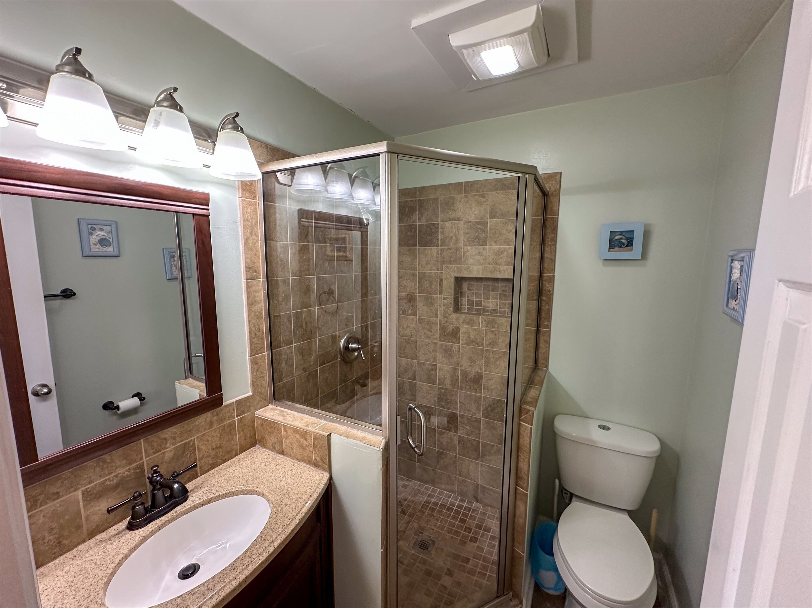 A bathroom with a glass-enclosed shower, a sink with a mirror, and a toilet.