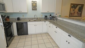 A kitchen with white cabinets, a granite countertop, a dishwasher, and a coffee maker. - Hatteras Heaven® - Oceanfront 2BR/2 Bath Condo - Pool, Renovated Kitchen, King  (Rodanthe)