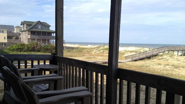 A wooden deck with chairs overlooking a beach and a boardwalk. - Hatteras Heaven® - Oceanfront 2BR/2 Bath Condo - Pool, Renovated Kitchen, King  (Rodanthe)
