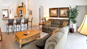 Ein Wohnzimmer mit einer Couch, einem Couchtisch und Stühlen. Es gibt eine Küchenzeile mit einem Herd und Schränken.