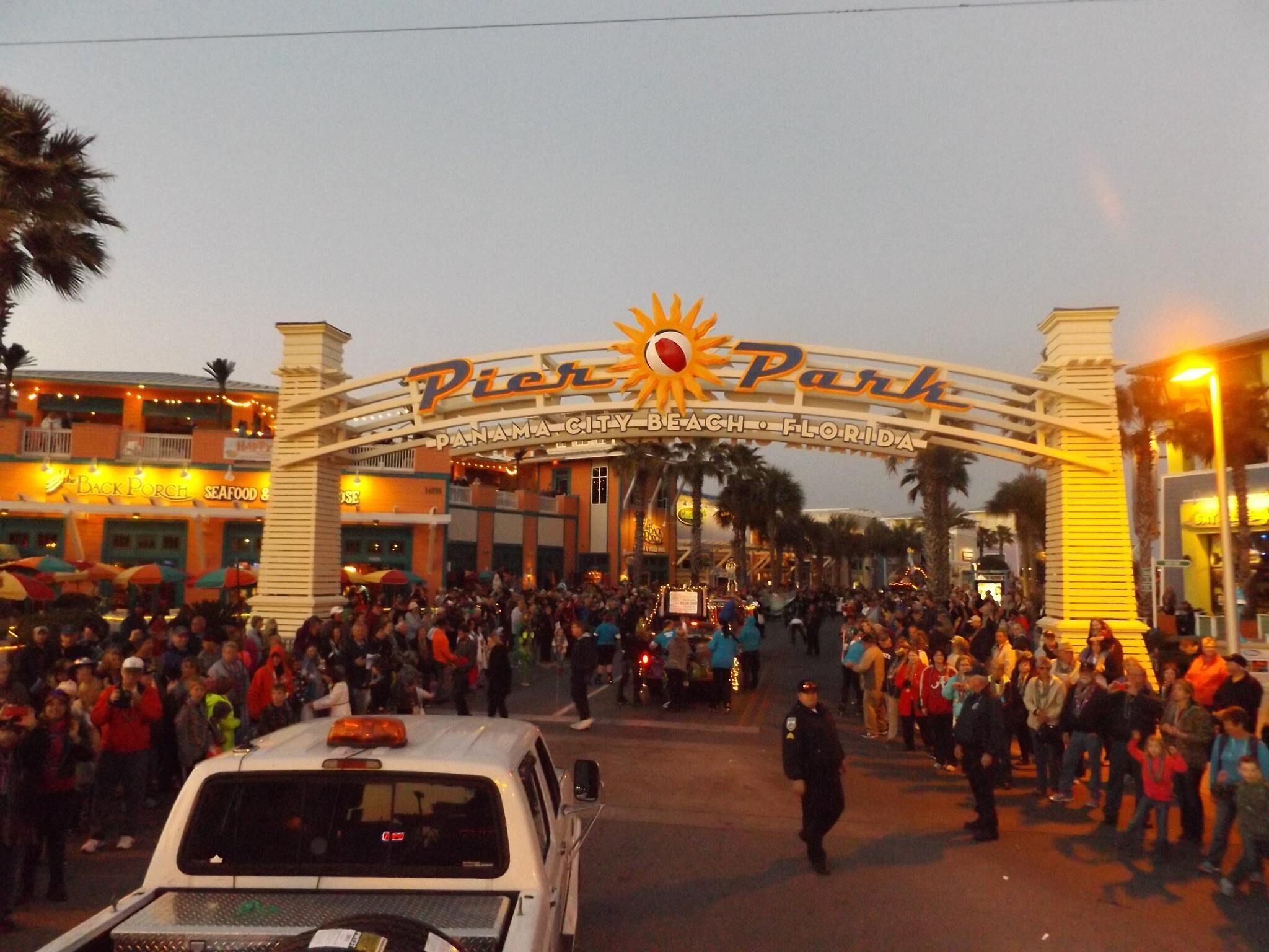 A crowded entrance to a theme park with a large archway and a sun emblem.