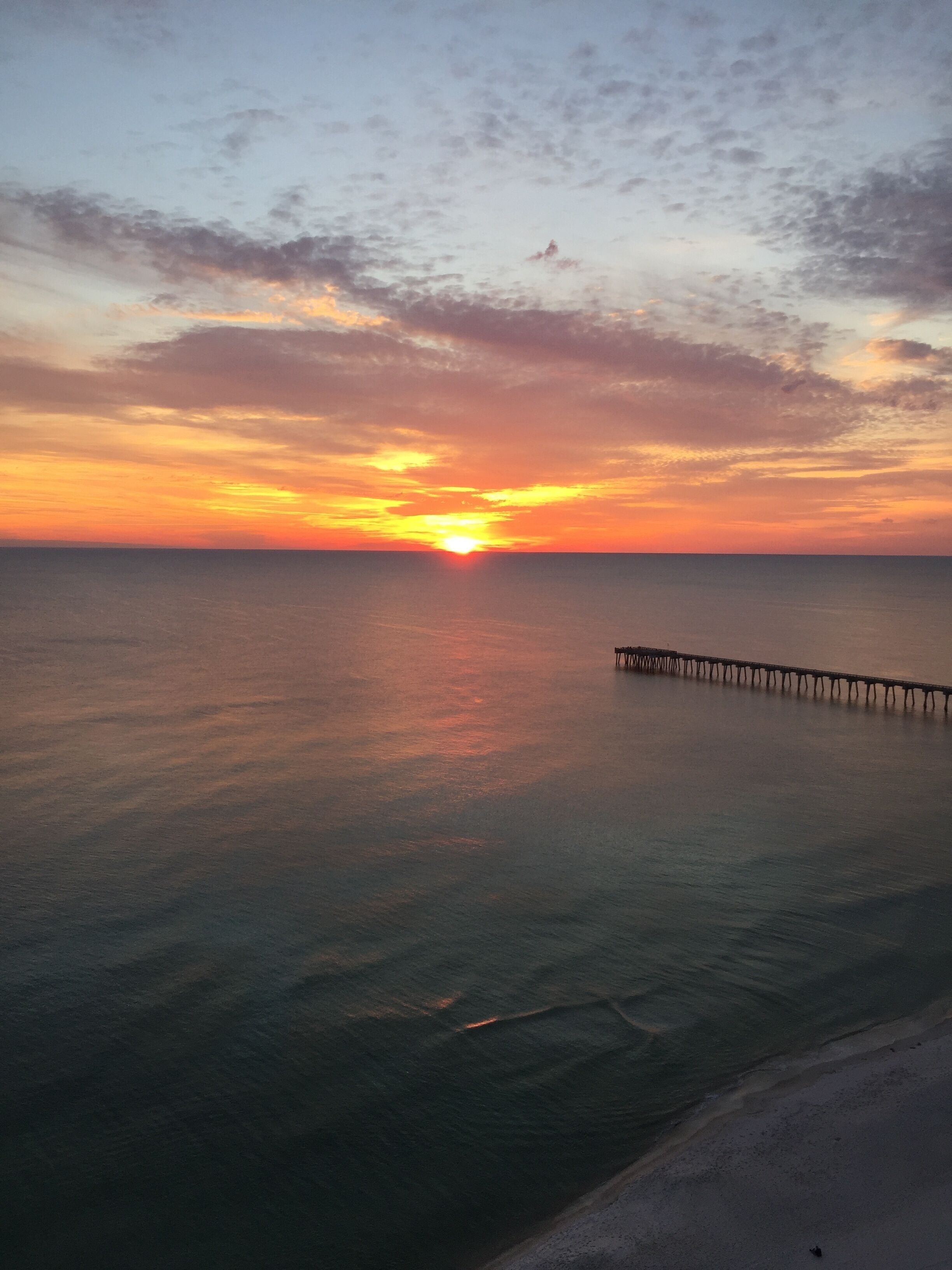 A sunset over a calm sea with a pier extending into the water.