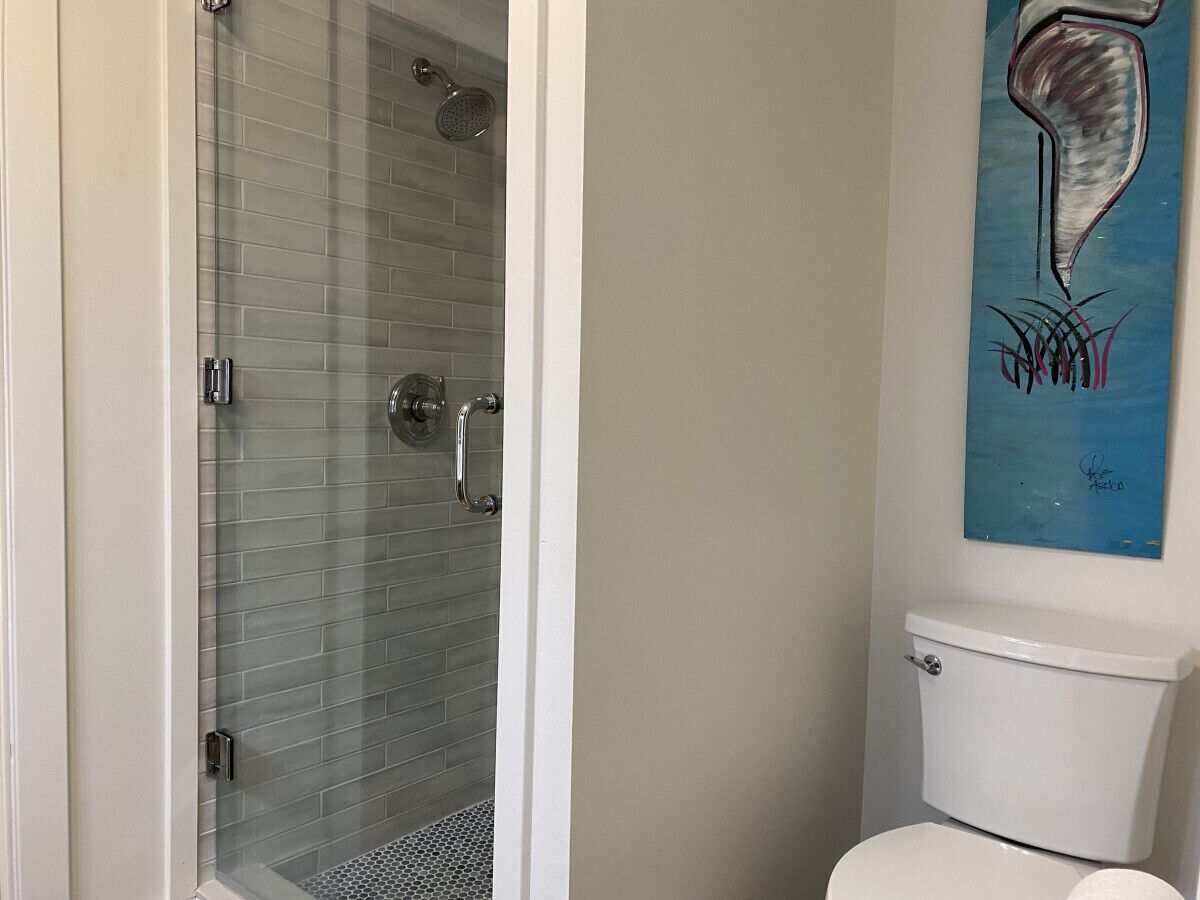 A bathroom with a glass shower enclosure, a white toilet, and a blue abstract painting on the wall.