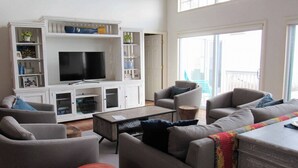 A living room with a TV, sofas, a coffee table, and a cabinet with shelves. - 476 Tarpon - Ocean Front - Full Time Beach (Fripp Island)