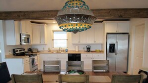 A kitchen with white cabinets, a stainless steel refrigerator, a microwave, and a coffee maker. There is a wooden dining table with four chairs. - 476 Tarpon - Ocean Front - Full Time Beach (Fripp Island)