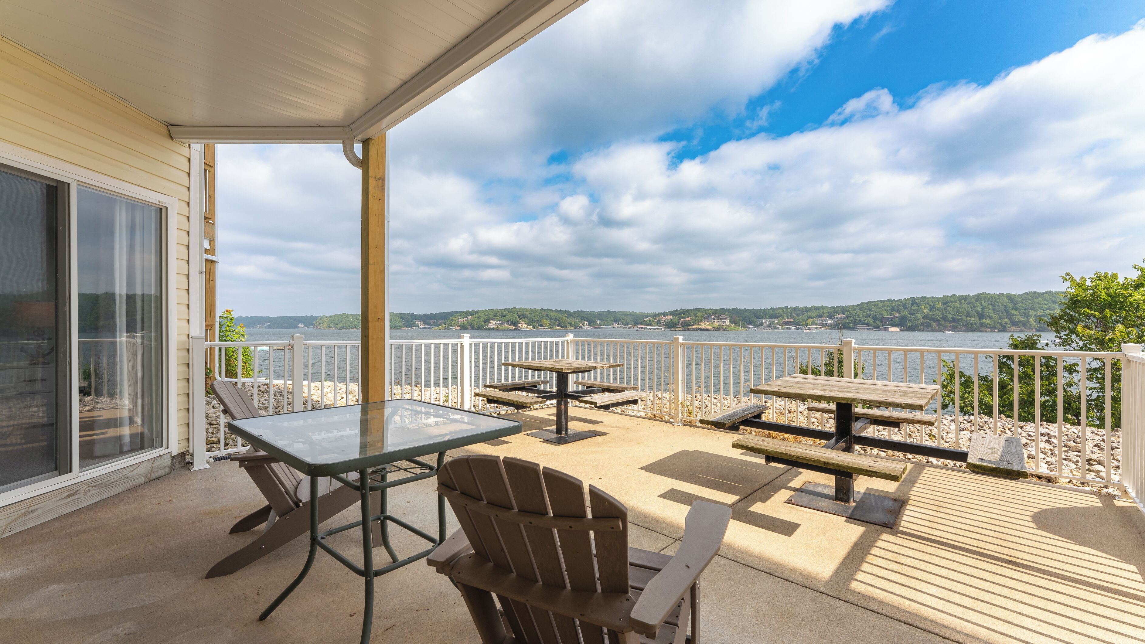 A covered outdoor area with a table and chairs, overlooking a body of water and a forested area.