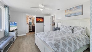 Een slaapkamer met een bed, een plafondventilator, een televisie en een schilderij.