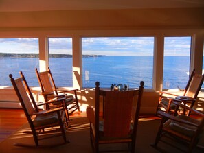 A room with a view of the sea through large windows, wooden rocking chairs, and a small table with a globe.