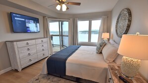 A bedroom with a bed, a dresser, a TV mounted on the wall, a window with a view, and a ceiling fan. - Building 10  BEAUTIFUL! MAIN CHANNEL-NEW 2 KING BEDs/2BA-SLEEPS 6
WIFI (Osage Beach)