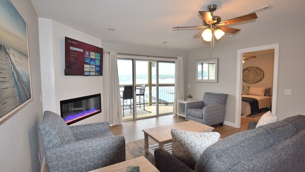 A living room with a fireplace, a ceiling fan, and a view of the outdoors. - Building 10  BEAUTIFUL! MAIN CHANNEL-NEW 2 KING BEDs/2BA-SLEEPS 6
WIFI (Osage Beach)