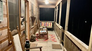 Une terrasse en bois avec un tapis à motifs floraux rouges, des chaises en bois et une lanterne.