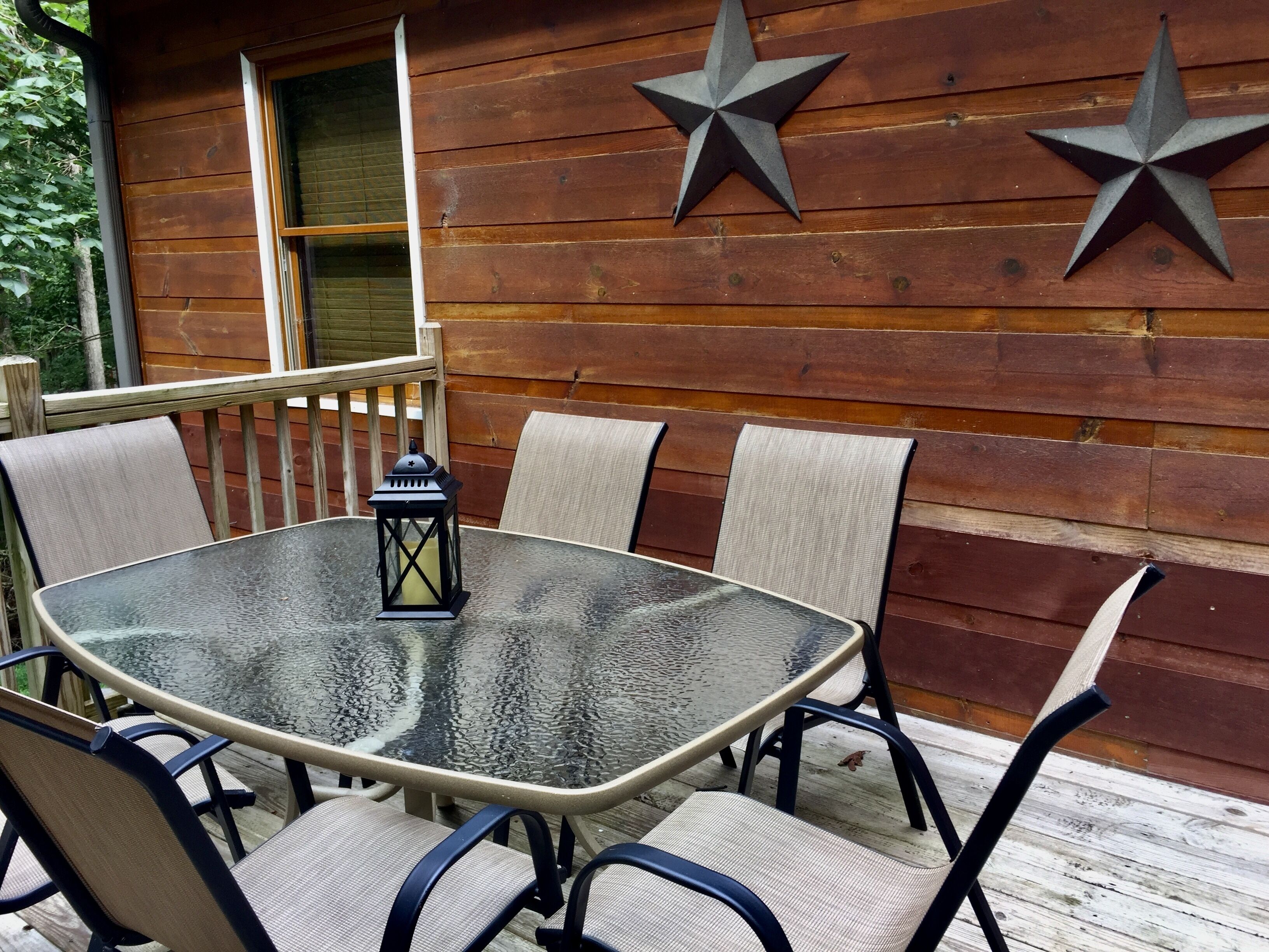 A wooden deck with a glass table and chairs, two star decorations on the wall, and a window with blinds.