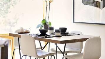 A dining area with a wooden table, white chairs, black and white cups, and a potted orchid.