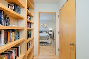 Un couloir étroit, avec des étagères en bois d’un côté et une chambre au bout.