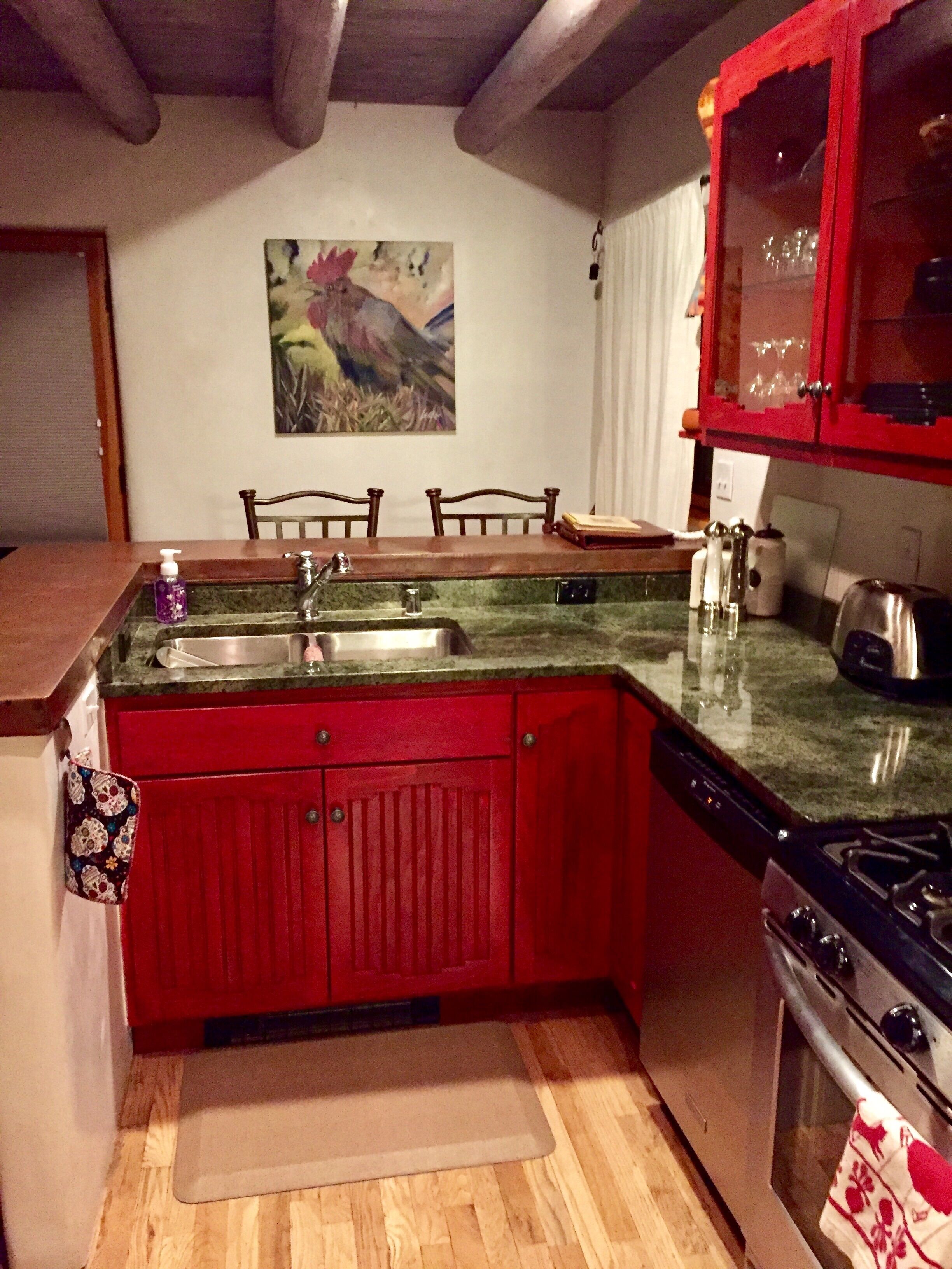 Una cocina con encimera de granito, armarios rojos, una estufa y un cuadro en la pared.
