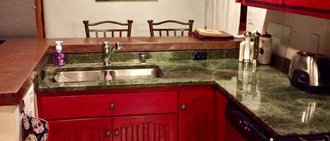 Una cocina con encimera de granito, armarios rojos, una estufa y un cuadro en la pared.